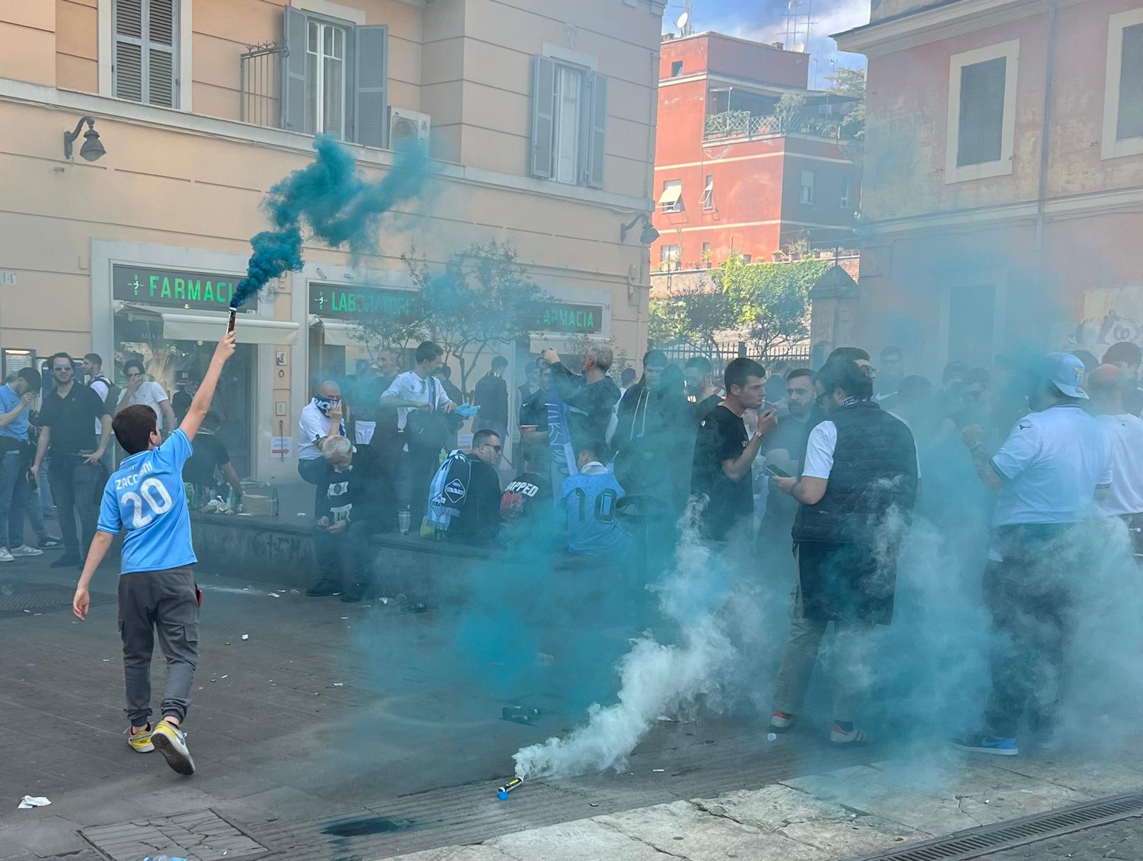 Young Lazio fan waving a flag and holding a flare, creating bright pyrotechnics at Ponte Milvio bridge in Rome.