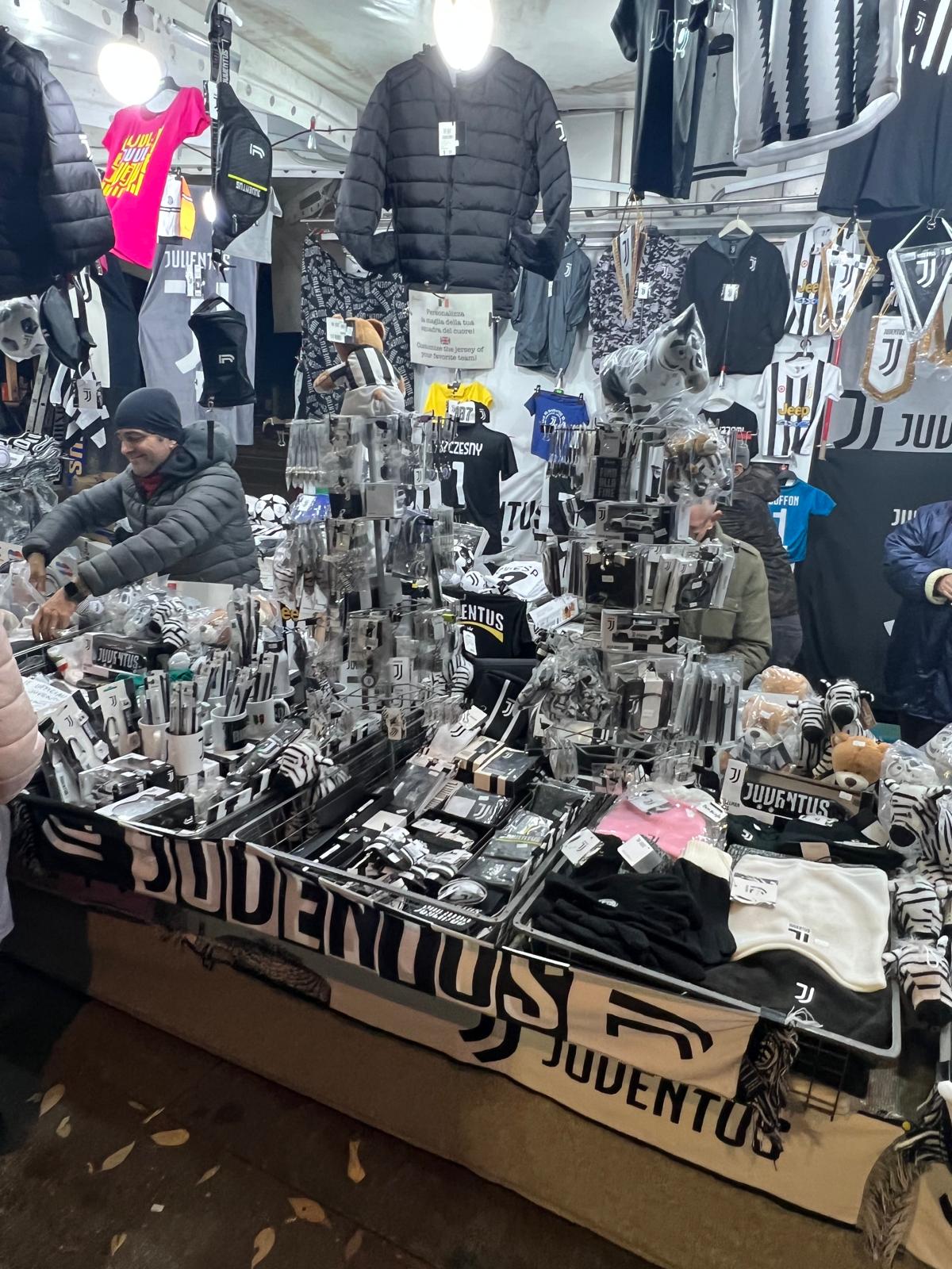 Juventus merchandise stand set up outside the Allianz Stadium in Turin, displaying black and white scarves, shirts, hats and official club souvenirs for sale to fans on matchday.