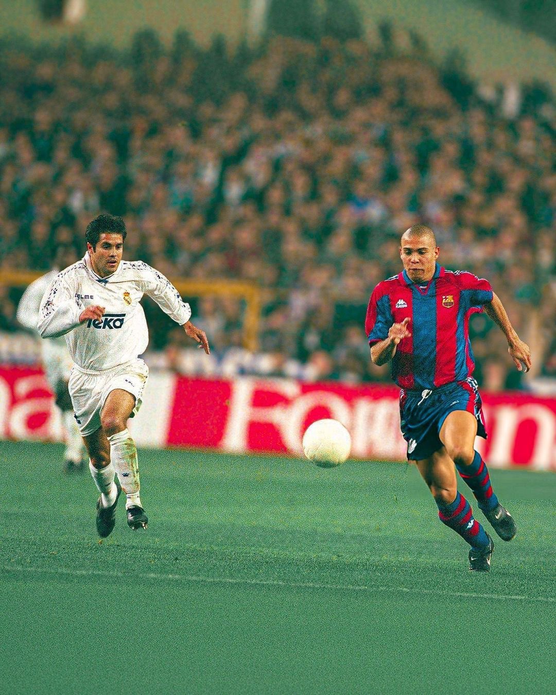A football action shot from the 1996–97 Real Madrid vs Barcelona match showing Carlos Secretario challenging Ronaldo Nazário on the wing.