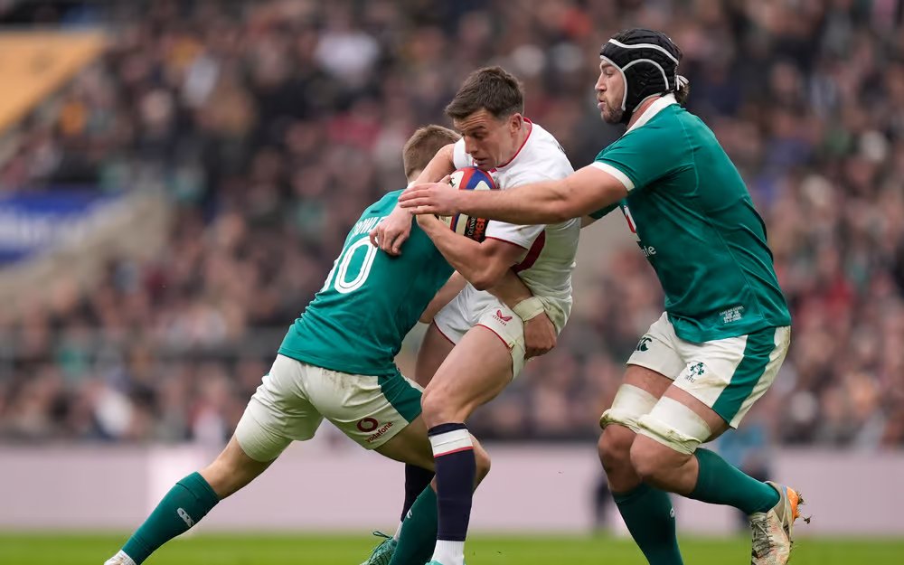 Two Ireland rugby players tackle an England ball carrier during Ireland’s record Six Nations victory at Twickenham, with the packed crowd in the background and the intensity of the collision capturing the dominance of the Irish defence.