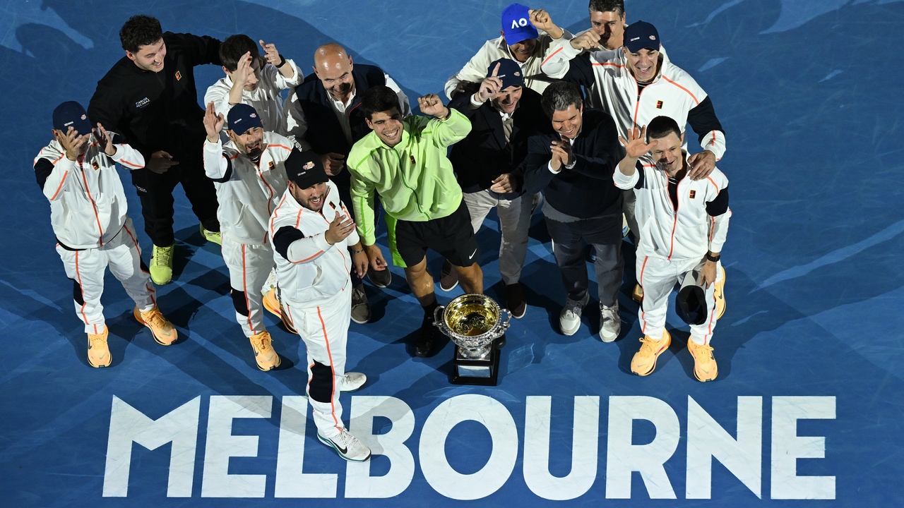 Carlos Alcaraz celebrating with the Australian Open trophy alongside his coaching team on court at Rod Laver Arena after winning the final.